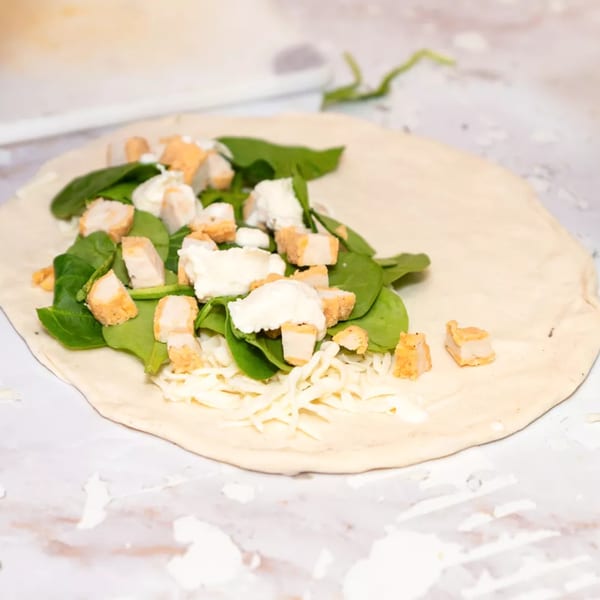 Unbaked Royal Pizza with spinach, chicken, mozzarella, and ricotta cheese on dough.