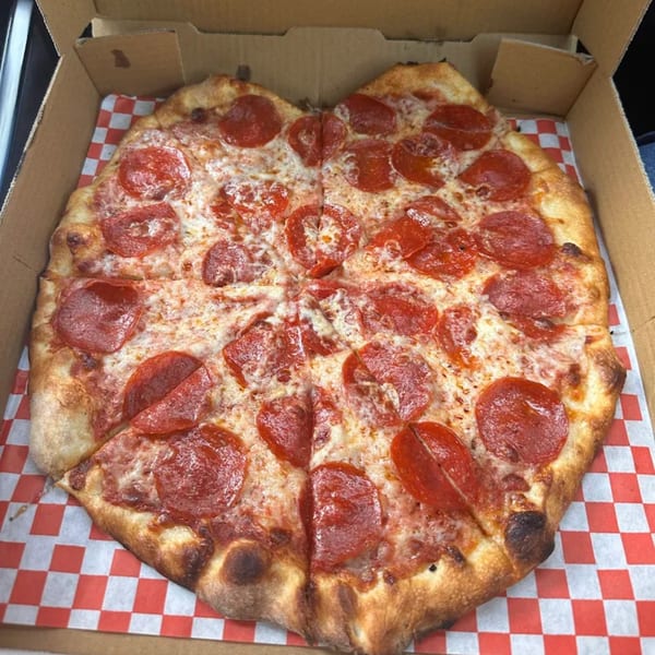 A Royal Pizza pepperoni pizza, cut into slices, in a cardboard box with red and white checkered paper.