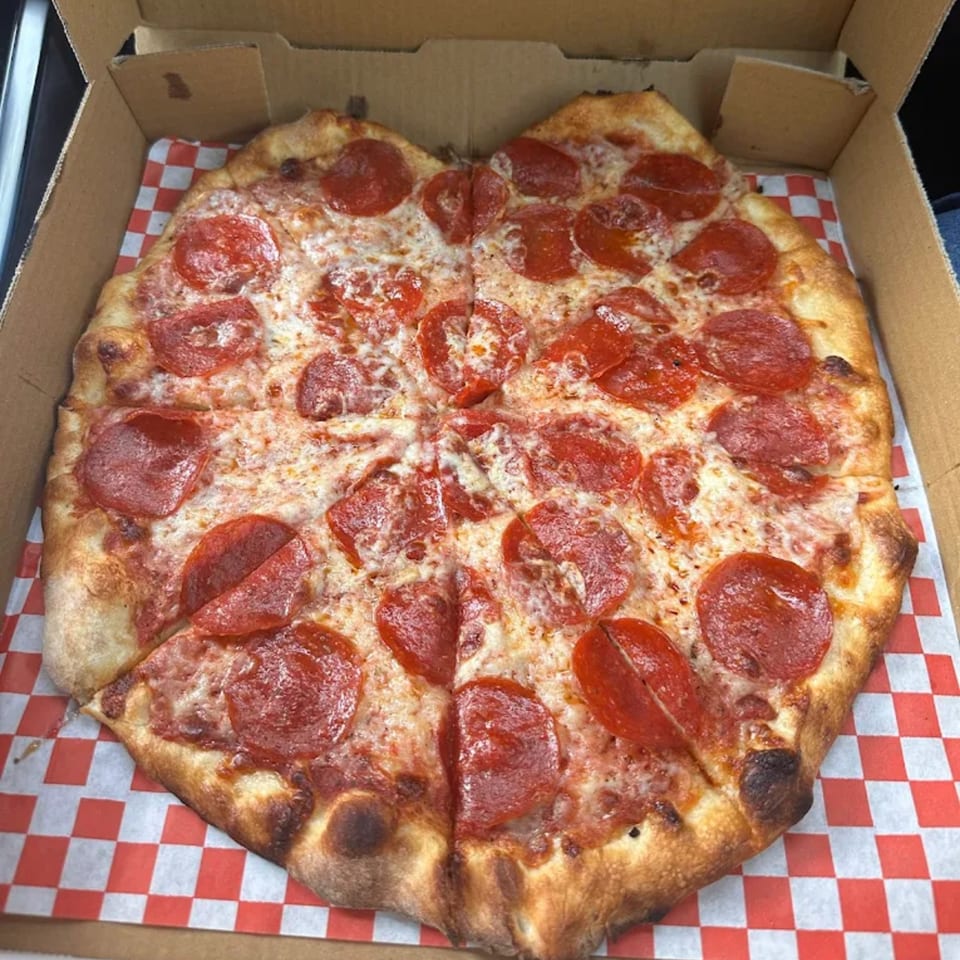 A Royal Pizza pepperoni pizza, cut into slices, in a cardboard box with red and white checkered paper.