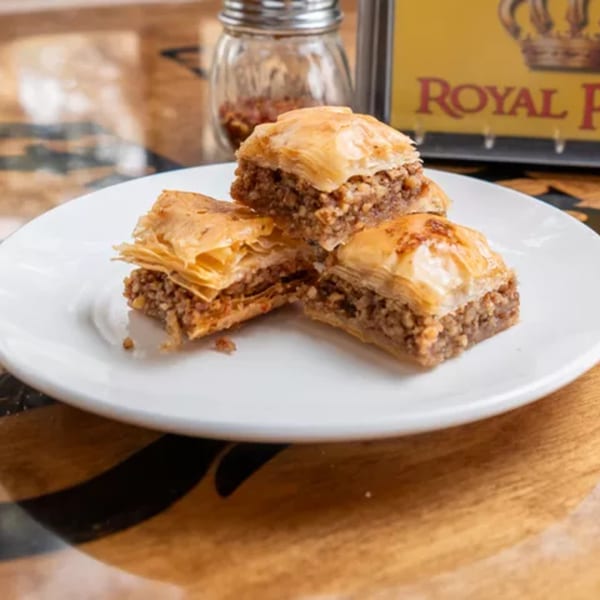 Three pieces of Royal Pizza's baklava on a white plate, with a spice shaker and logo in the background.