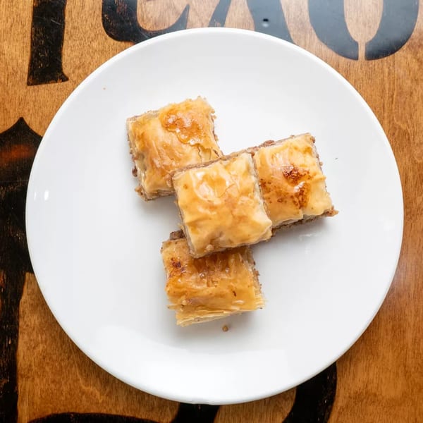Four pieces of baklava with honey glaze on a white plate, on a wooden table.