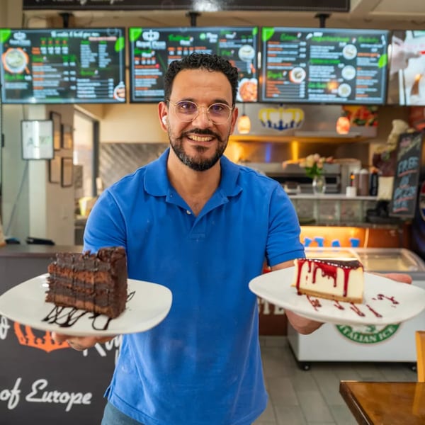 Smiling Royal Pizza staff member holding a slice of chocolate cake and a slice of cheesecake.