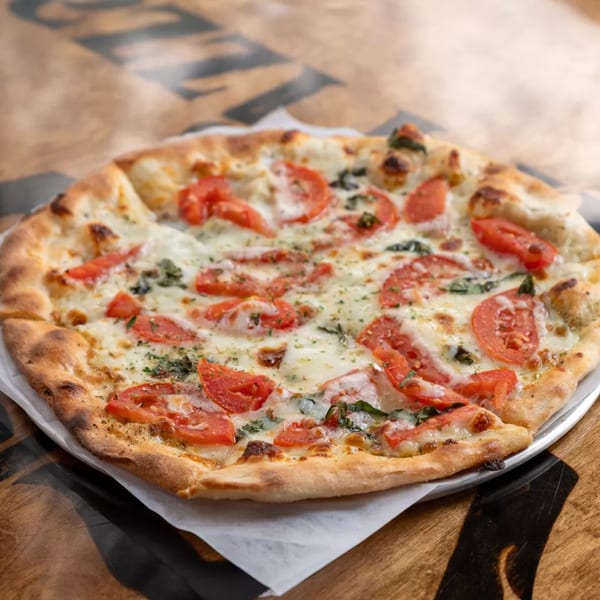 Royal Pizza's Margherita pizza with sliced tomatoes, mozzarella, and basil on a wooden table.